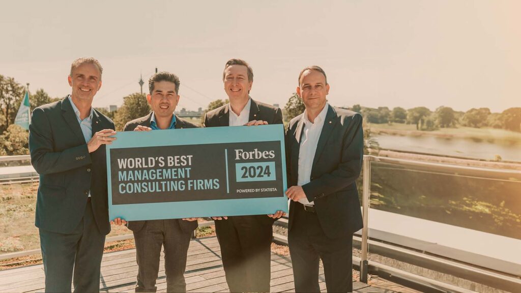 Four men hold a sign reading &#039;World&#039;s Best Management Consultancies 2024&#039; by Forbes.