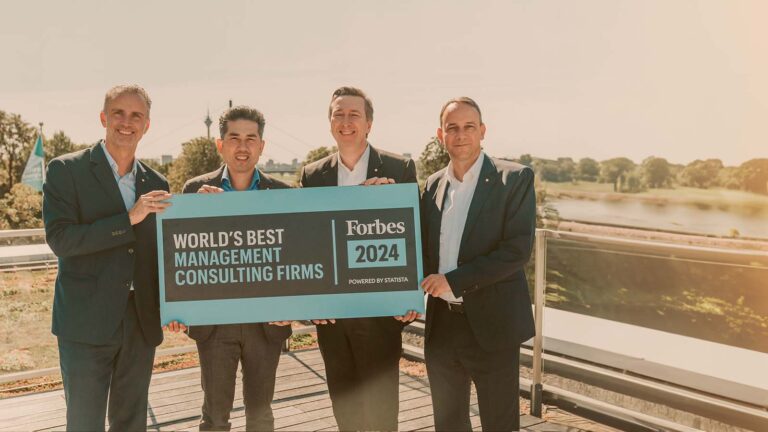 Four men hold a sign reading &#039;World&#039;s Best Management Consultancies 2024&#039; by Forbes.