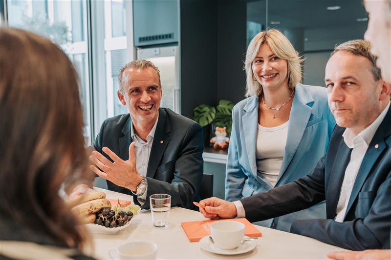 Eine Gruppe von Personen in einem modernen Büro, die an einem Tisch sitzen und miteinander sprechen.