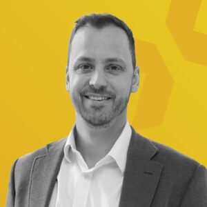 Porträt von Josh Berry in einem grauen Anzug vor einem gelben Hintergrund.