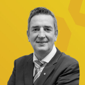 Porträt von Jürgen Hübner vor einem gelben Hintergrund.
