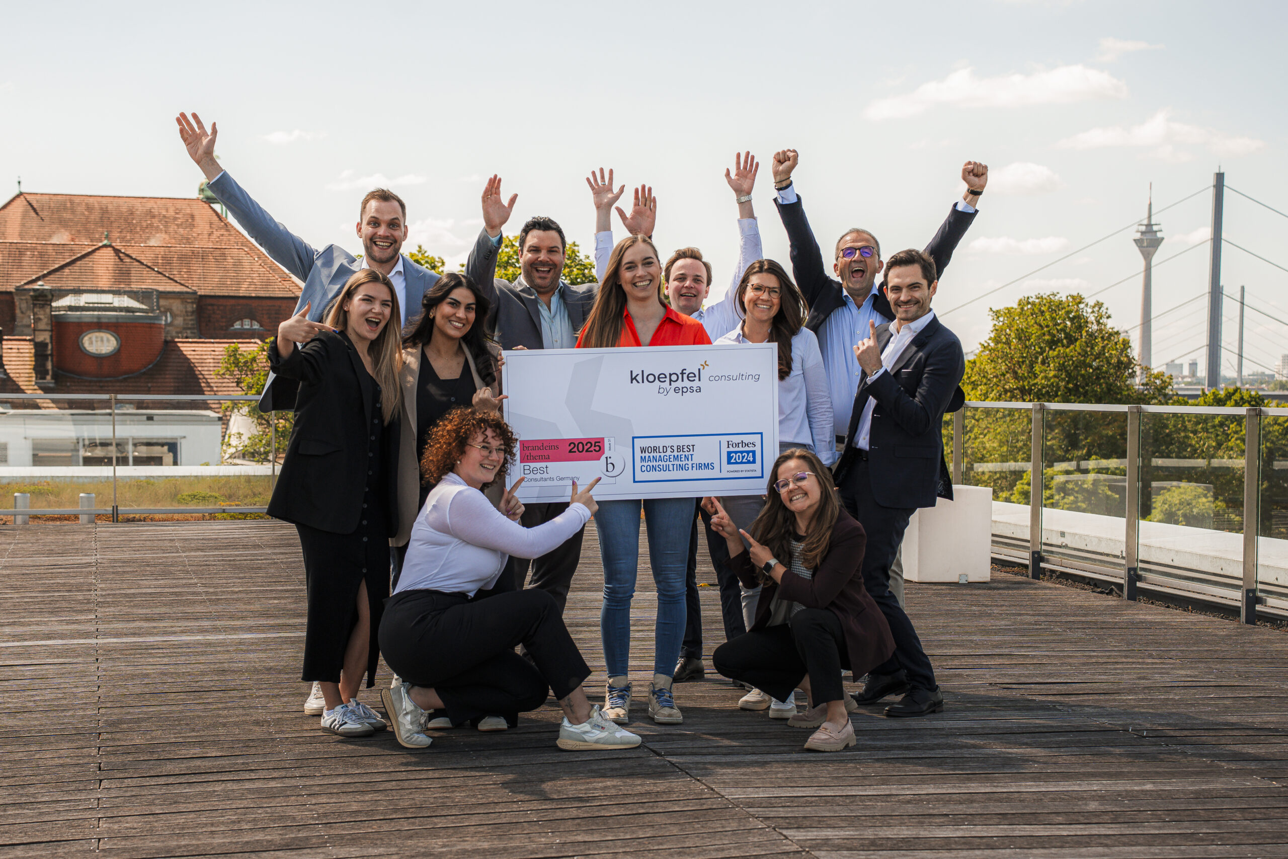 Gruppenfoto von Kloepfel-Mitarbeitern, die eine Auszeichnung in den Händen halten und jubeln.