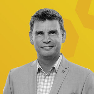 Porträt von Andy McBrine in einem grauen Anzug vor gelbem Hintergrund.