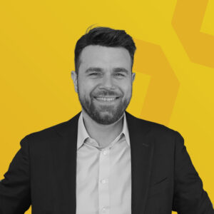 Porträt von Frank Wischnewski in einem Anzug vor einem gelben Hintergrund.