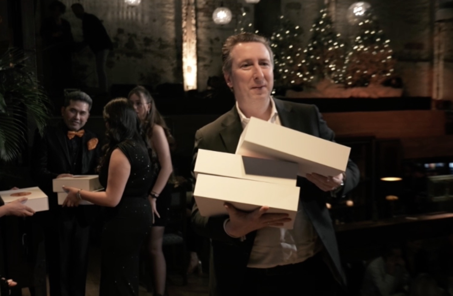 Mann trägt mehrere weiße Geschenkboxen in einer festlichen Umgebung.