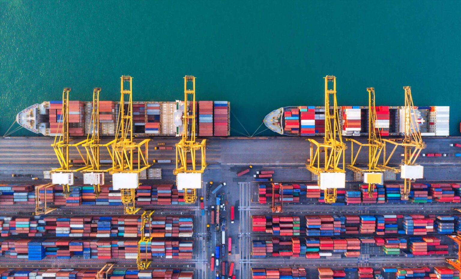Luftaufnahme eines Containerterminals mit Kränen und mehreren Schiffen im Hafen.