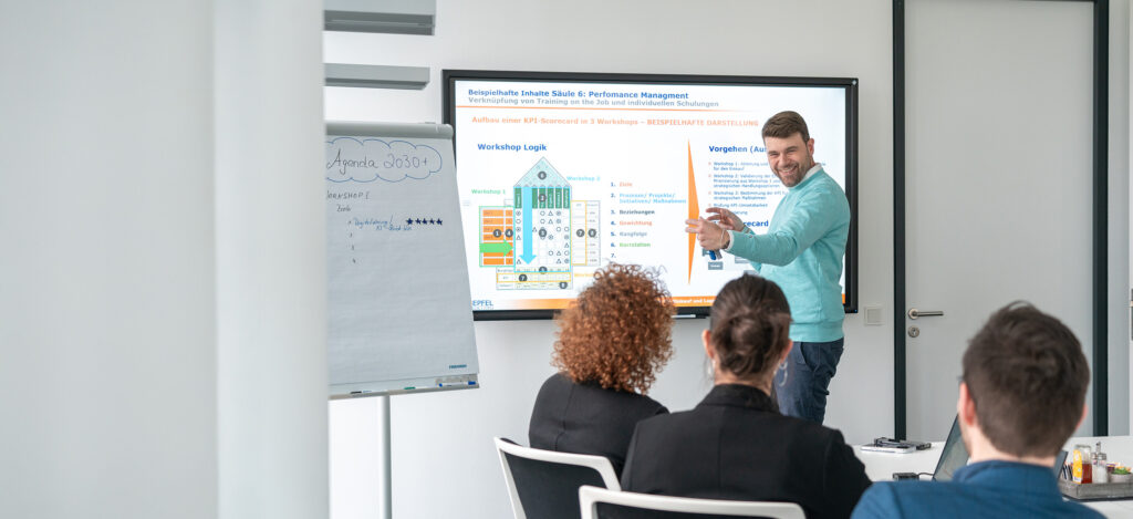 Un homme fait une présentation pendant un atelier avec un flipchart et un écran en arrière-plan.