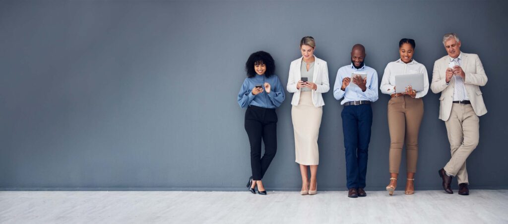 Five people stand next to each other and use mobile devices in a neutral room.