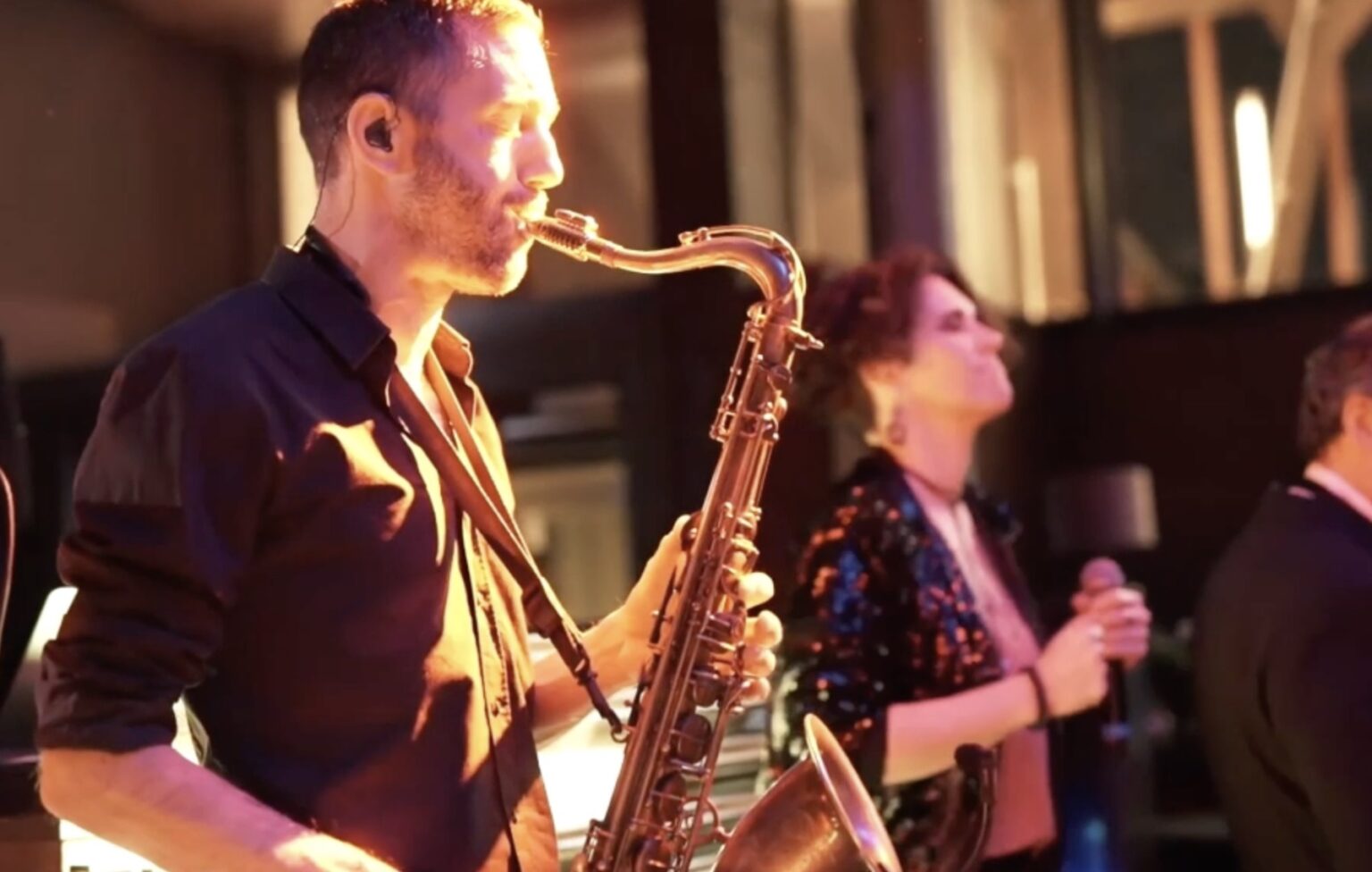 Saxophonist spielt Saxophon während einer Live-Performance mit Sängerin im Hintergrund.