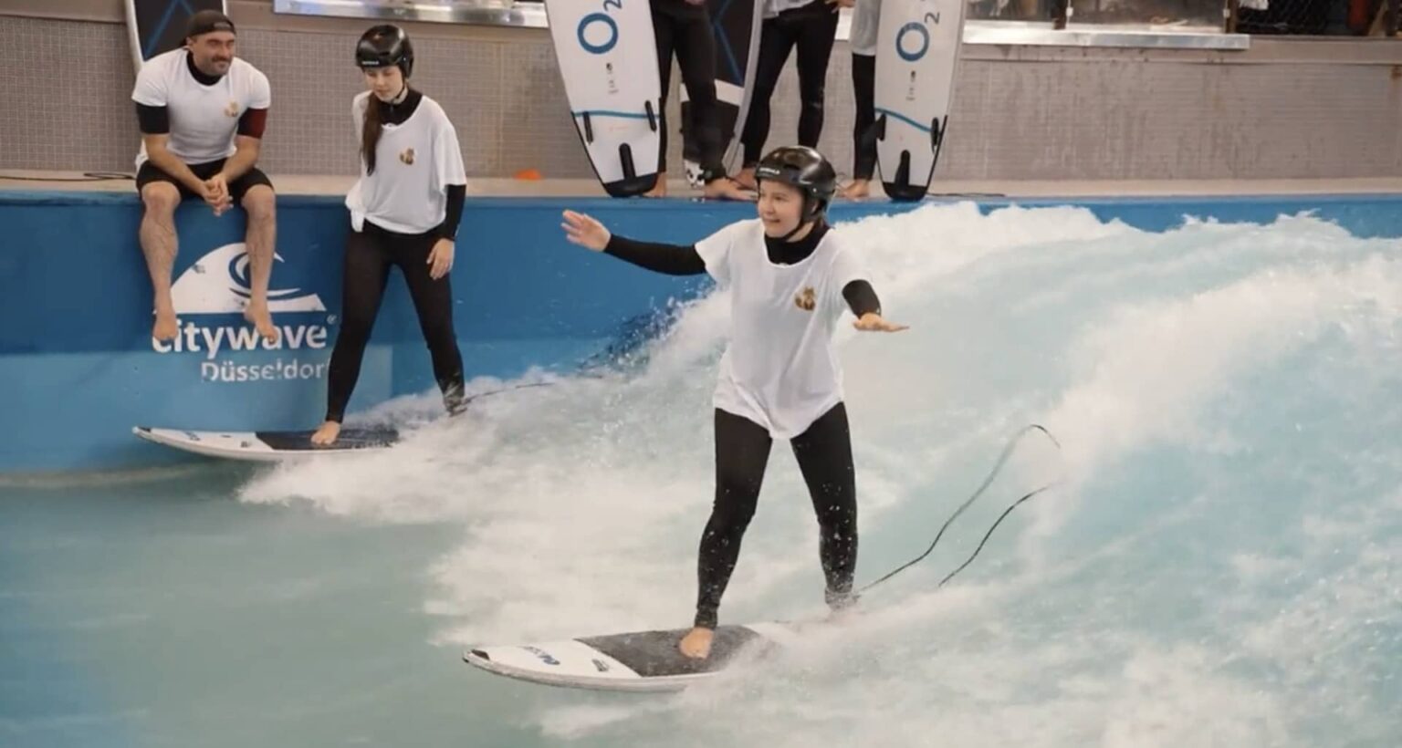 Eine Surferin steht auf einem Surfbrett und reitet eine Welle in einer Indoor-Surfanlage in Düsseldorf.
