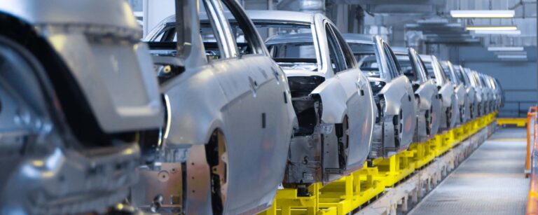 Reihe von unvollständigen Automobilkarosserien auf einem Montageband in einer Fertigungshalle.