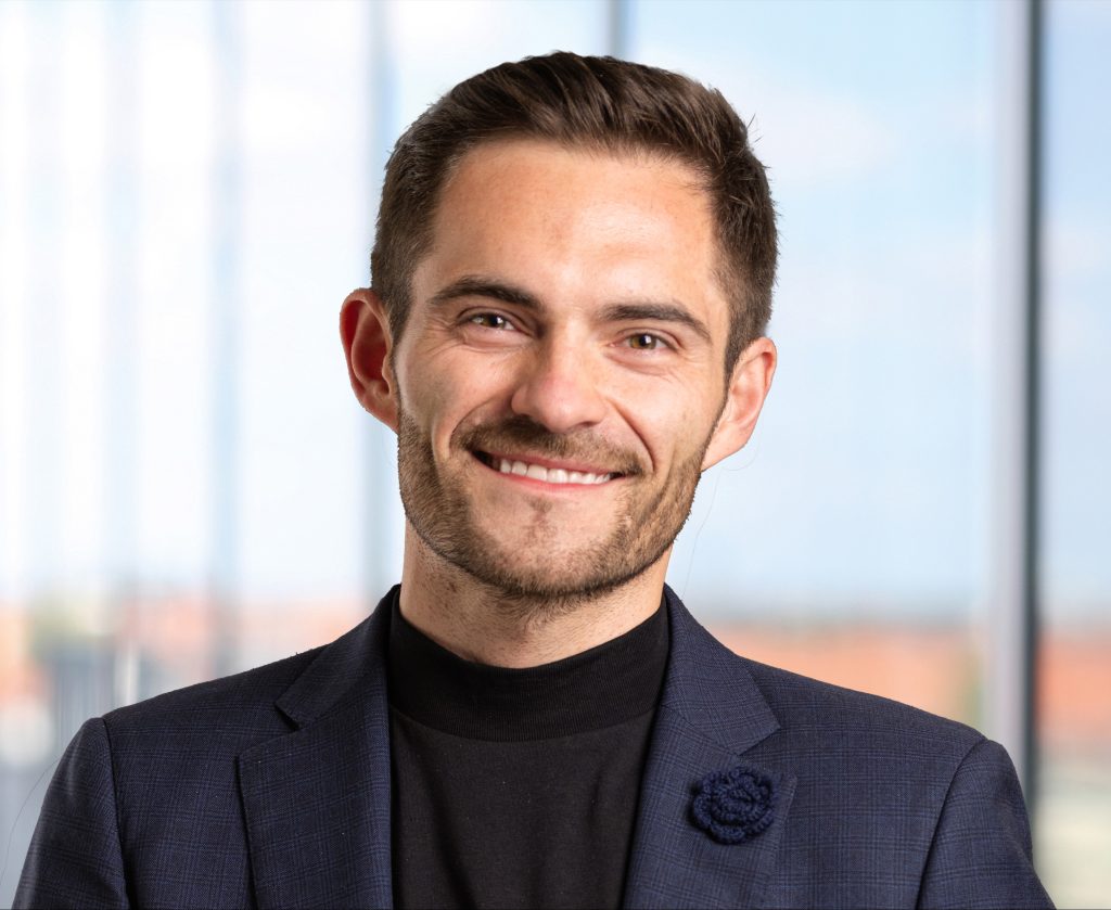 Daniel Sperling lächelt in einem Anzug mit schwarzem Rollkragenpullover vor einem hellen Hintergrund.