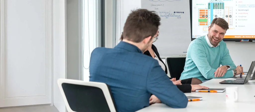 Eine Gruppe von Personen in einem Konferenzraum, die an einem Tisch sitzen und diskutieren.