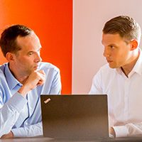 Zwei Männer im Gespräch vor einem Laptop Zwei Männer in einem Gespräch, während sie vor einem Laptop sitzen.